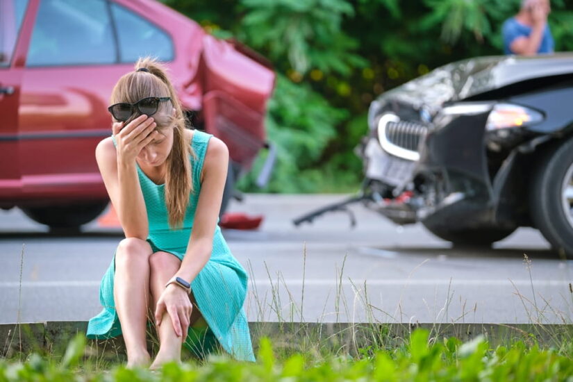 Visibly Upset Woman Sitting On A Curb Next To A Car Crash Scene