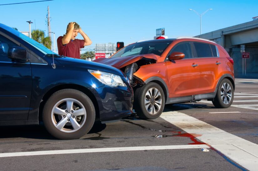 Man Holding His Head In Shock Standing Next To A Car Crash Scene