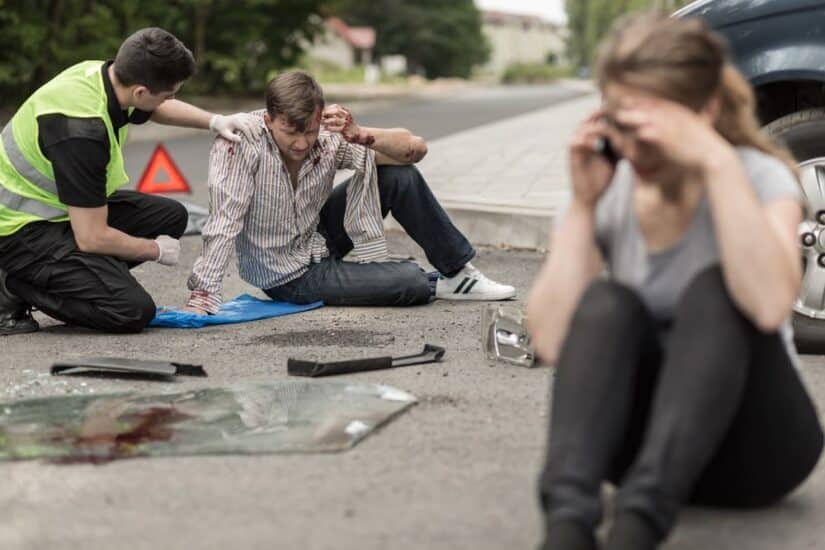 Man Sitting On The Ground And A Woman Calling On The Phone Next To A Car Crash Scene