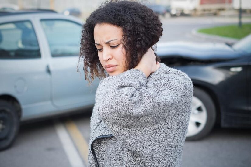 Woman Holding Her nEck In Pain Next To A Car Crash Scene